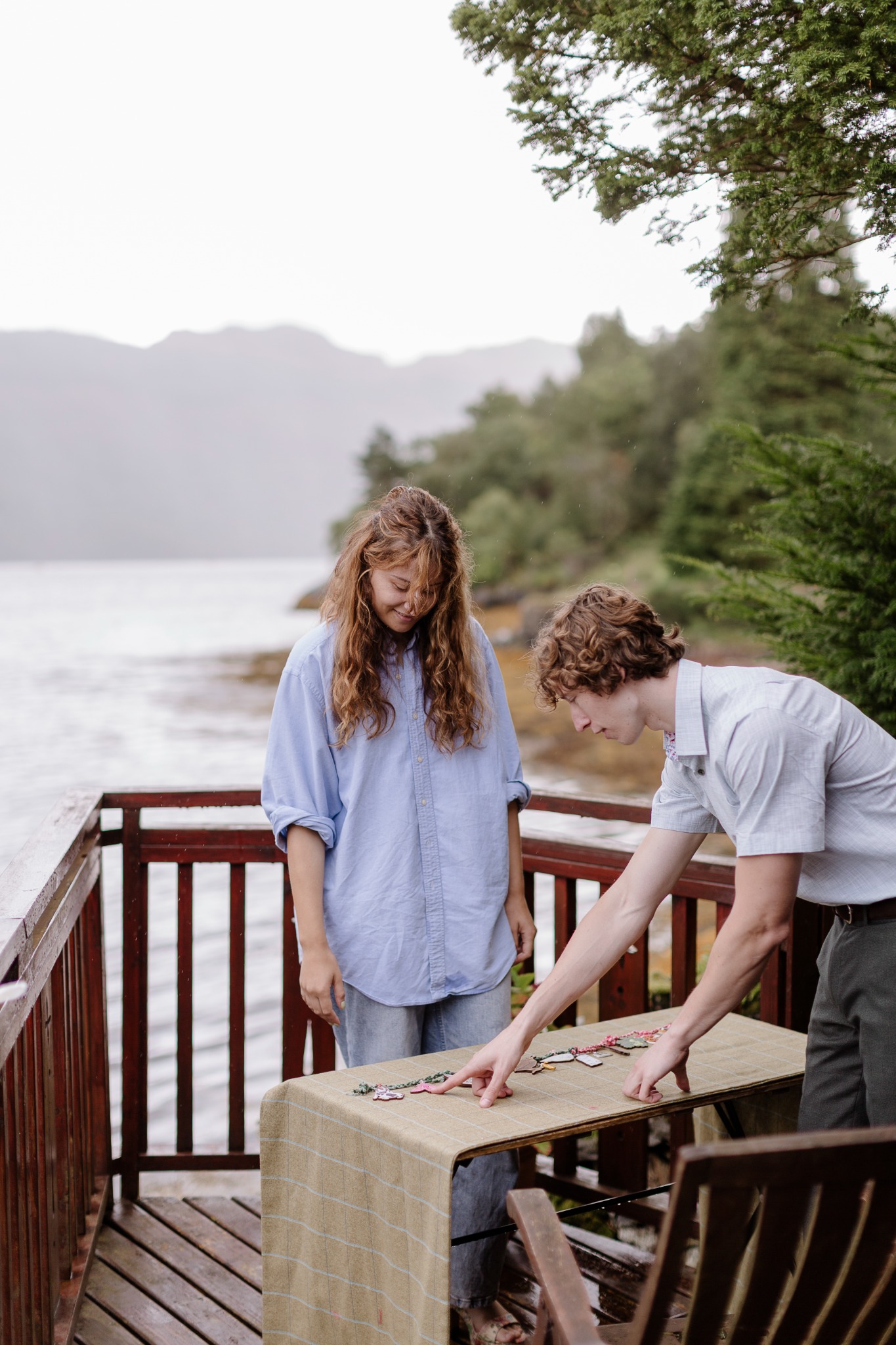 Two people arranging small objects on a table beside a lake.